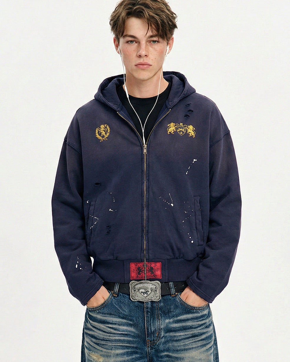 Front view of model wearing a navy blue distressed zip up hoodie with paint splatter accents and hooded neck.