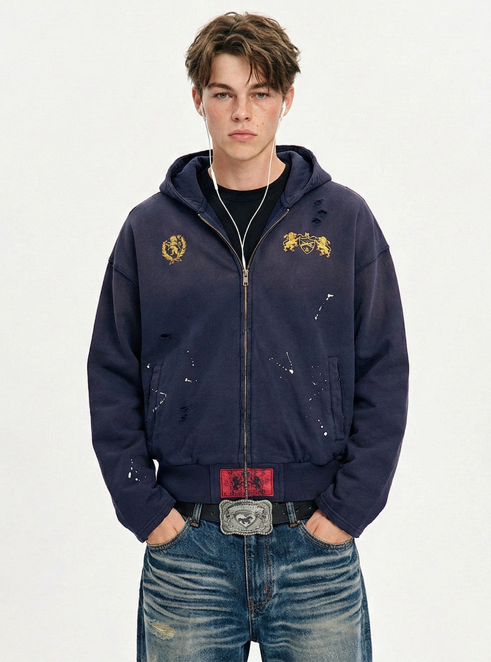 Front view of model wearing a navy blue distressed zip up hoodie with paint splatter accents and hooded neck.