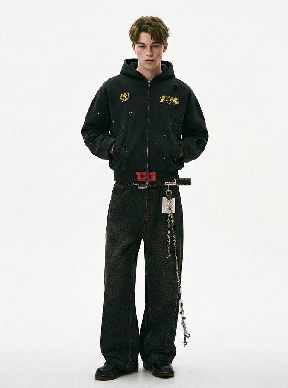 Full length view of model styling a washed black distressed zip up hoodie with wide leg printed jeans and boots.