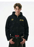 Half body shot of model wearing a washed black cotton zip hoodie featuring paint splatters and drop shoulder fit.