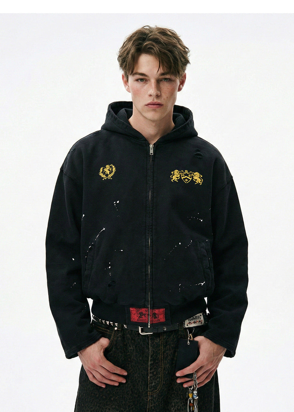 Half body shot of model wearing a washed black cotton zip hoodie featuring paint splatters and drop shoulder fit.