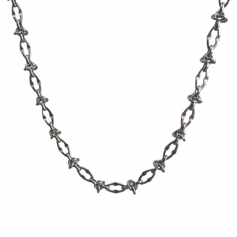 Close-up of silver barbed wire necklace with angular twisted links on white background.