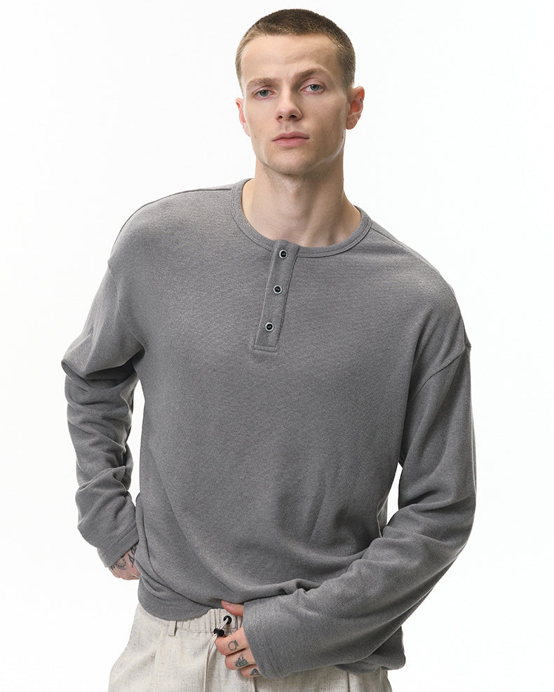 Man wearing a gray long-sleeve henley shirt on a white background