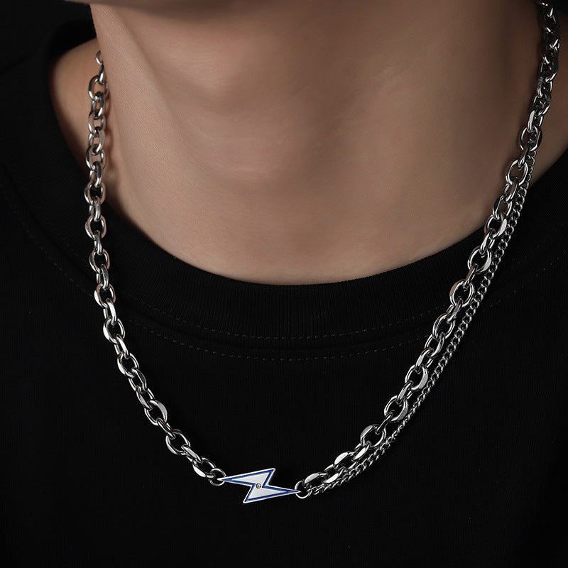 Man wears layered silver chain necklace with lightning bolt pendant.