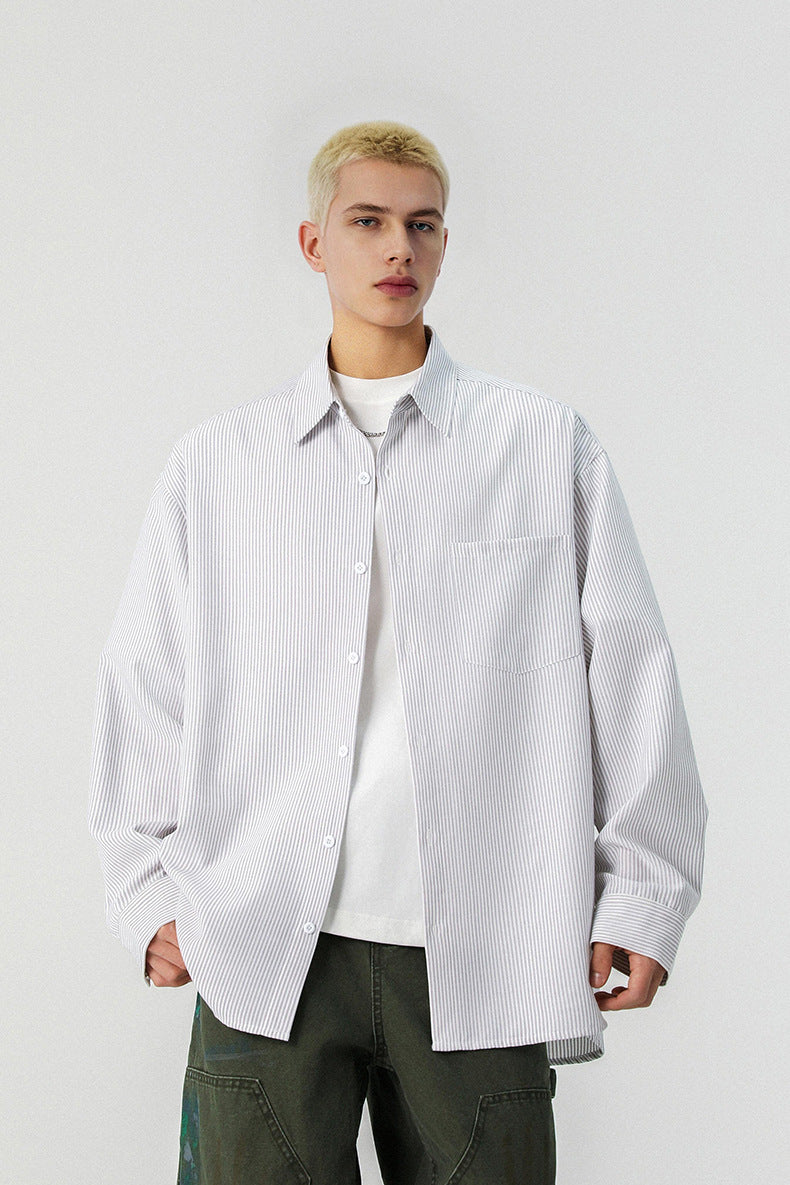 Medium shot of model wearing an unbuttoned grey vertical striped long sleeve shirt over white tee.