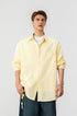 Half length shot of model styled in an unbuttoned yellow pinstripe collared shirt with blue jeans.