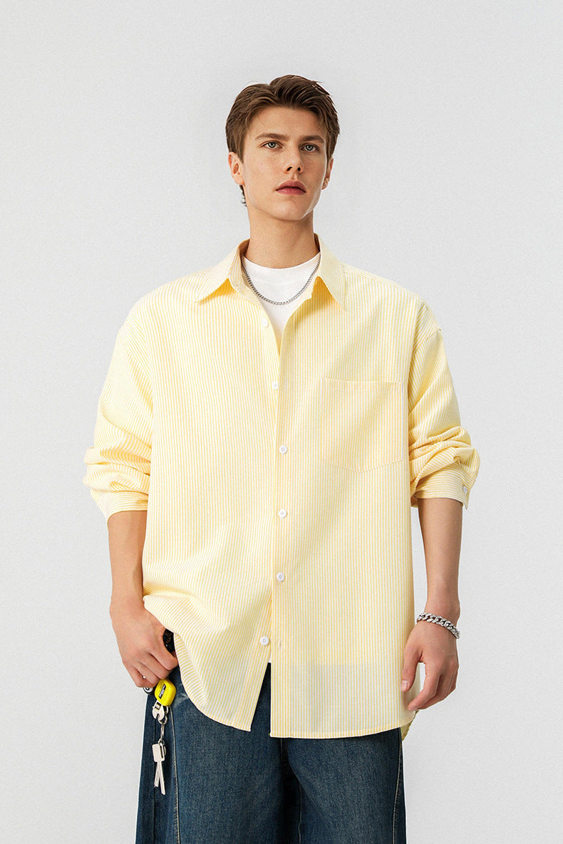 Half length shot of model styled in an unbuttoned yellow pinstripe collared shirt with blue jeans.
