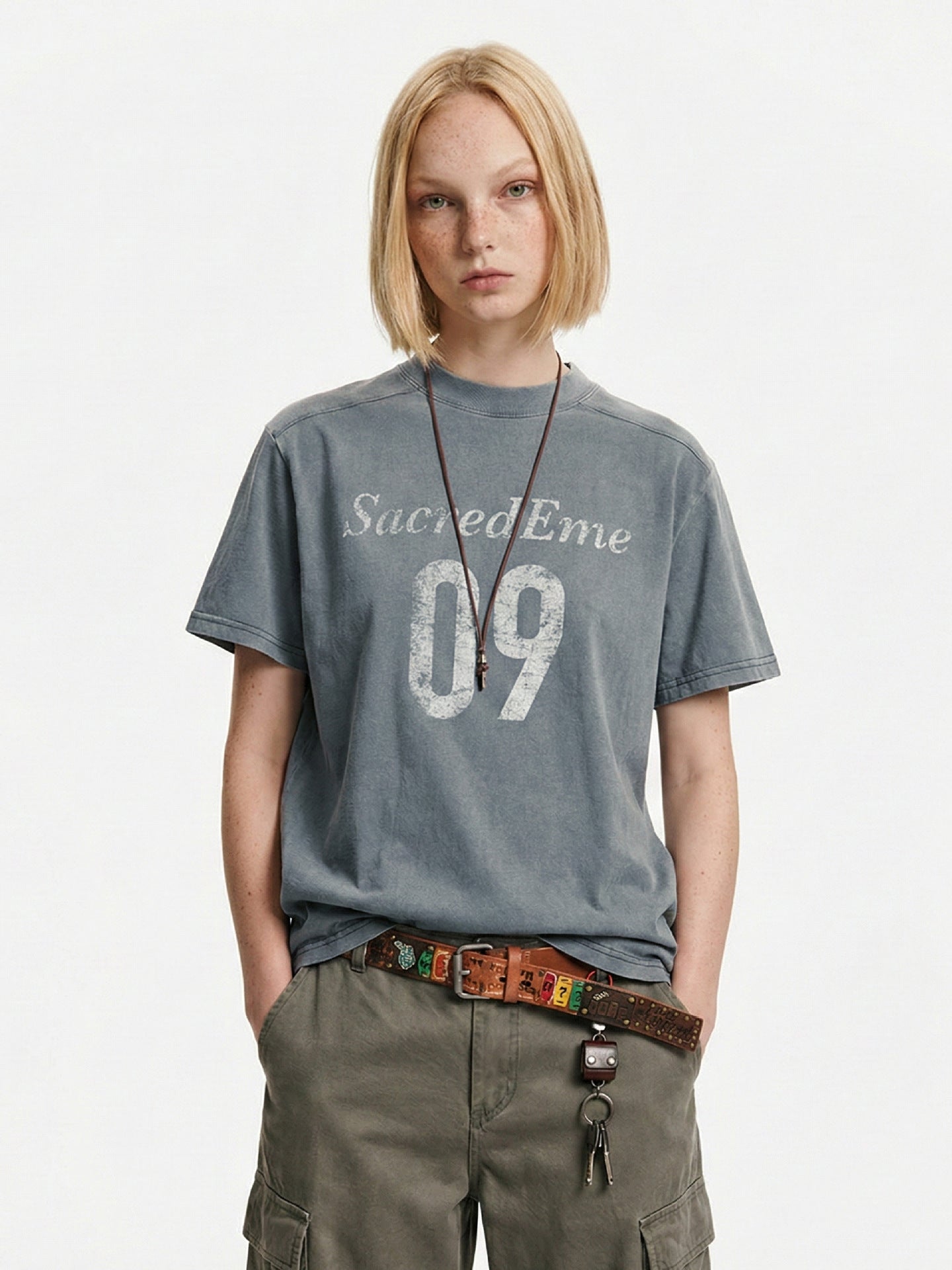 Blue-gray varsity graphic T-shirt styled with olive cargo pants and a leather belt.