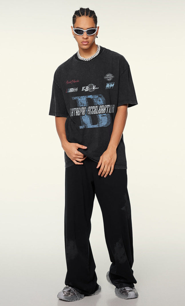 Model poses in black tee with racing print and wide-leg pants.