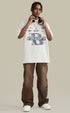 Model wearing white graphic tee with brown pants and headphones.