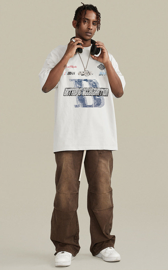 Model wearing white graphic tee with brown pants and headphones.