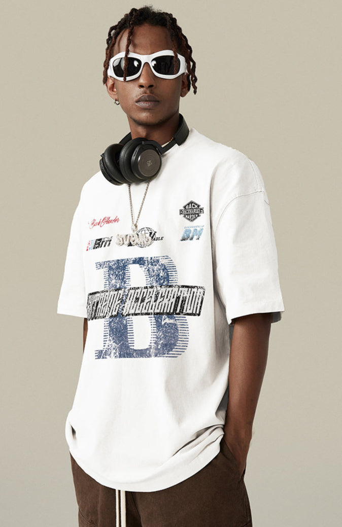 Model wearing white graphic tee with brown pants and headphones.
