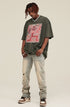 Model wearing olive green graphic tee with graffiti skeleton and distressed jeans.