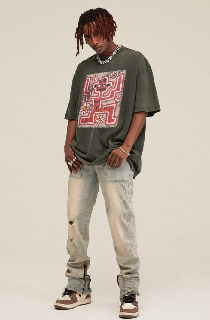 Model wearing olive green graphic tee with graffiti skeleton and distressed jeans.