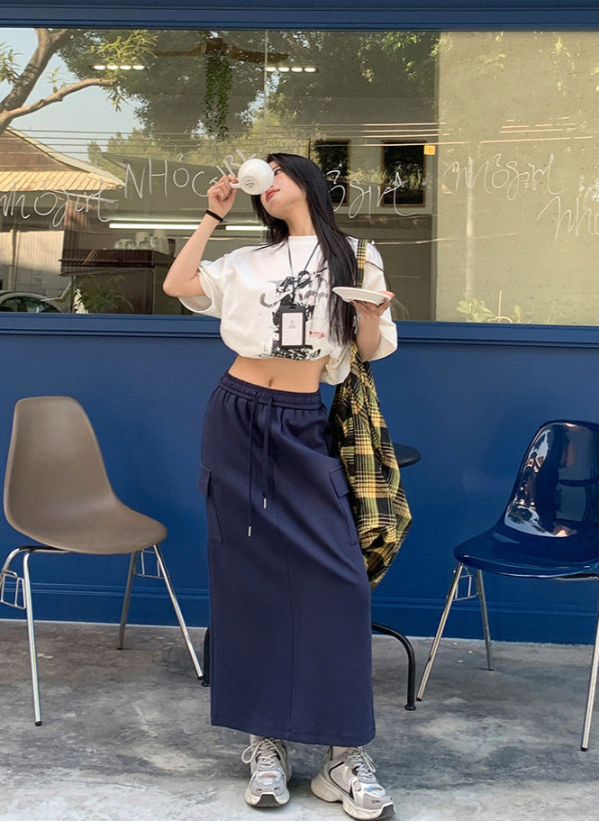 Model drinks coffee outside cafe in navy drawstring maxi skirt and printed cropped tee.
