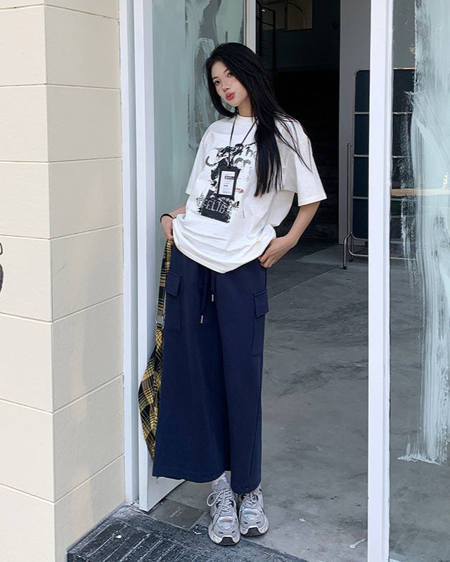 Model poses at doorway in navy maxi skirt with cargo pockets, graphic tee, and chunky sneakers.