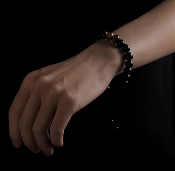 Hand wears black obsidian bracelet with tiger eye beads.