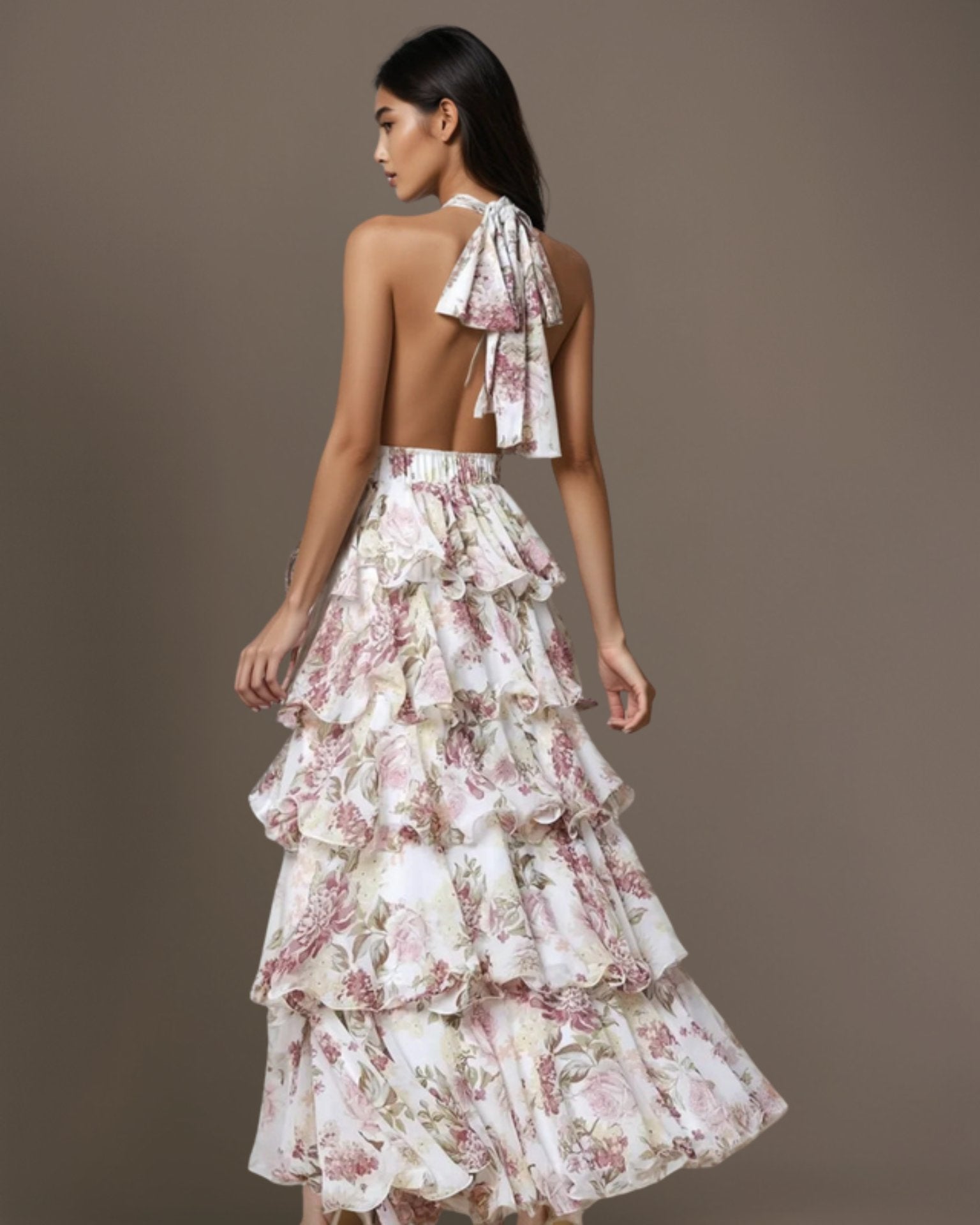 Back view of woman wearing an off-white halter floral dress with a gray background