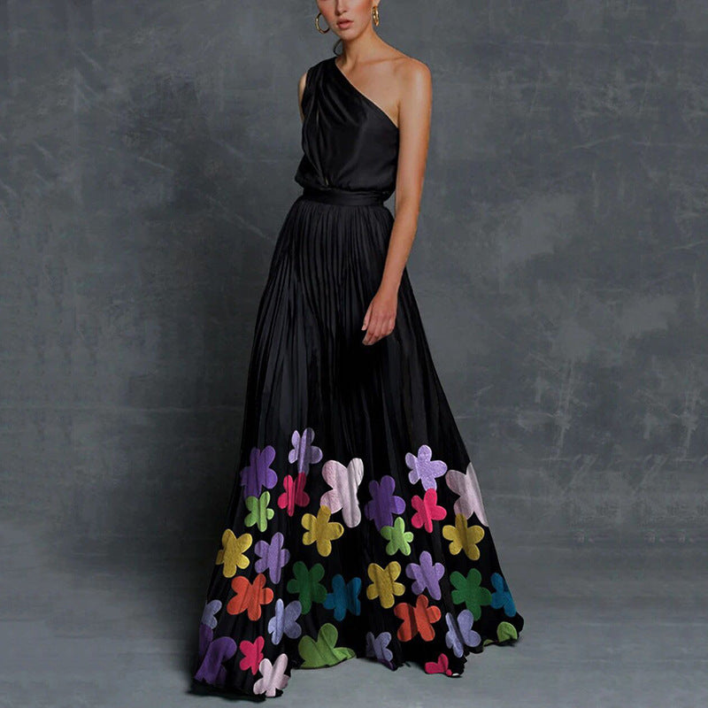 Woman wearing a black one-shoulder maxi dress with colorful floral patterns on a gray background