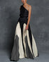 Woman wearing a black, white, and gray one-shoulder maxi dress against a gray background