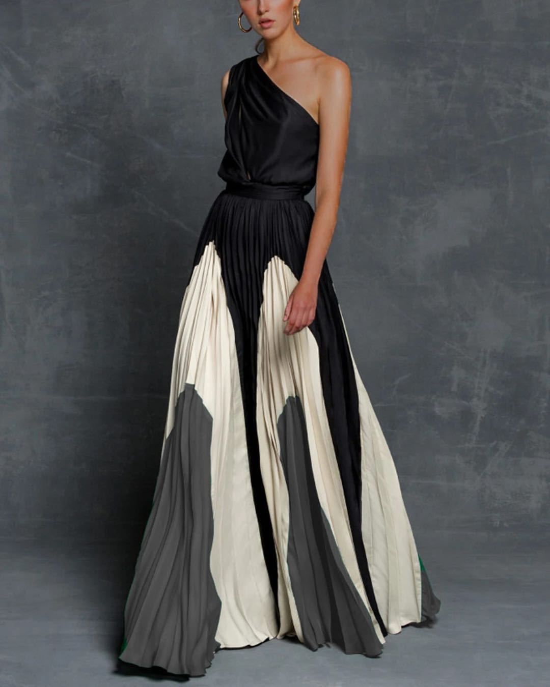 Woman wearing a black, white, and gray one-shoulder maxi dress against a gray background
