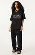 Woman in black oversized Ouroboros 8-ball t-shirt and dark pants.