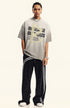 Model wears light gray oversized T-shirt with motivational text and taped arrow print, styled with black track pants.