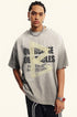 Light gray tee with “Overcome Obstacles” message and faded yellow arrow, styled in a streetwear look.