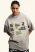 Male model stares ahead wearing oversized grey graphic tee with inspirational message.