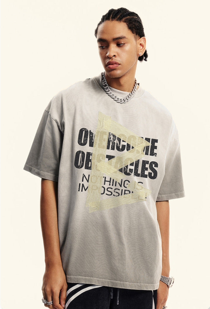 Model looks sideways wearing grey T-shirt with cracked type and yellow arrow print.