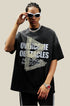 Man in black oversized tee with bold text and arrow design, wearing white sunglasses and a chunky silver chain.