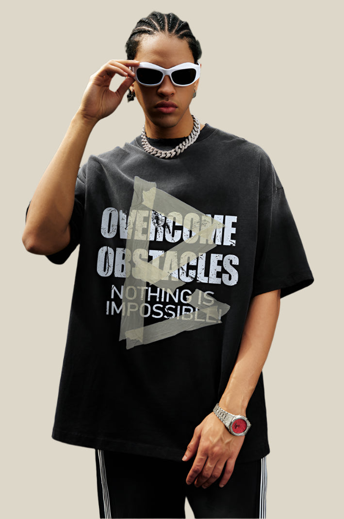 Man in black oversized tee with bold text and arrow design, wearing white sunglasses and a chunky silver chain.