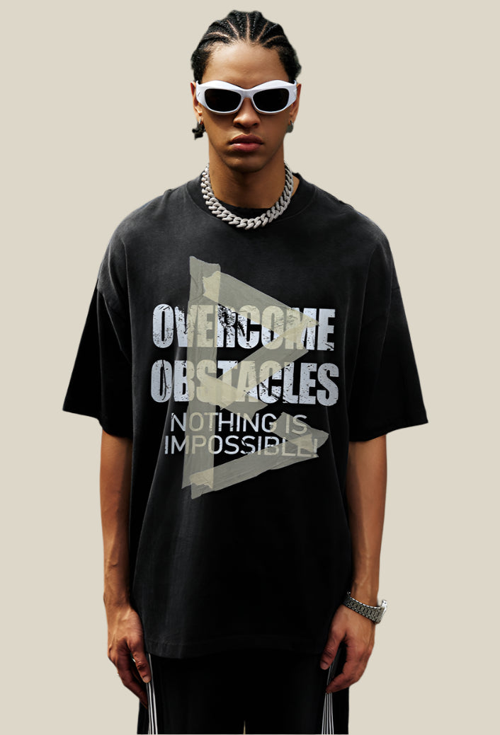 Front-facing model wears washed black tee with cracked motivational text and large yellow arrow graphic.