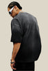 Back of a washed black oversized tee with no print, worn by male model with braided hair.