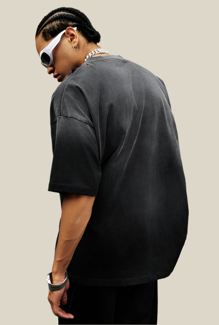 Back of a washed black oversized tee with no print, worn by male model with braided hair.