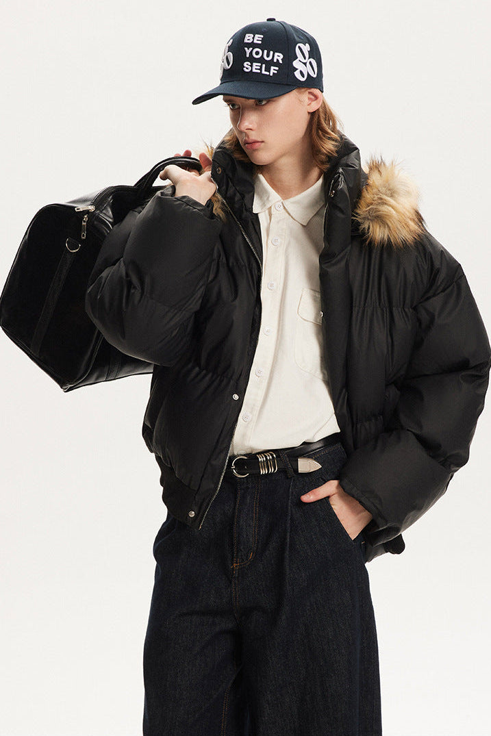 Three-quarter view of model wearing a black boxy winter jacket carrying a black duffel bag.
