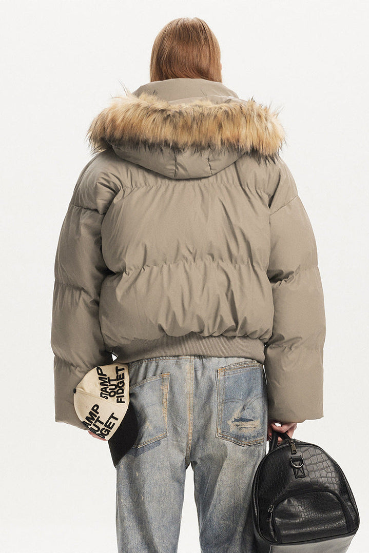 Back view of model wearing a short khaki quilted puffer coat featuring a wide faux fur lined hood.