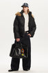 Full length view of model styled in a black oversized puffer jacket with brown fur hood trim.