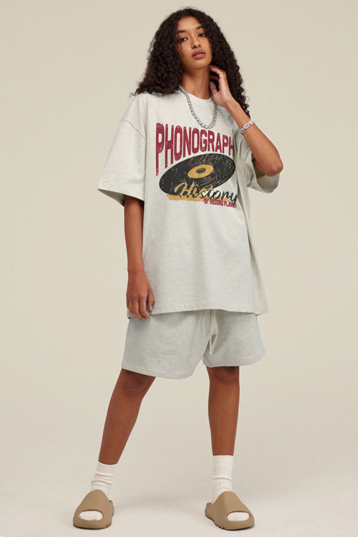 Woman in light grey phonograph tee posing at an angle.