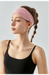 Woman wearing a wide light pink headband and black sports top, side profile.