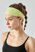 Woman wearing a wide pixie green headband and black sports top in side profile.