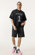Model wears oversized black T-shirt with 'Raise Fares' and number 1 print, styled with matching shorts and pink sneakers.
