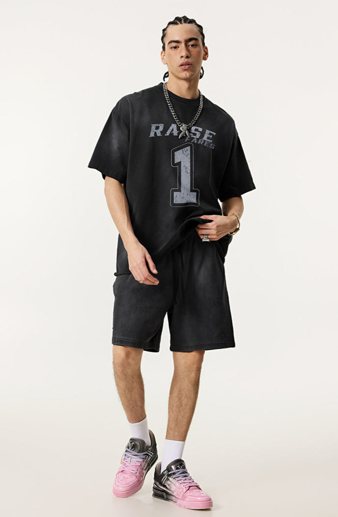 Model wears oversized black T-shirt with 'Raise Fares' and number 1 print, styled with matching shorts and pink sneakers.