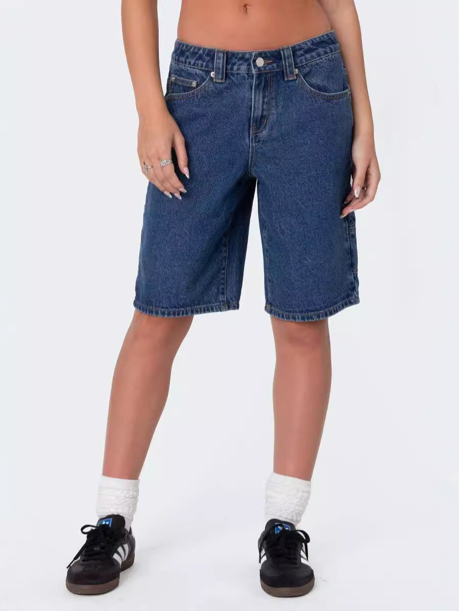 Front view of woman wearing plain dark wash knee-length denim shorts paired with black sneakers and white socks.