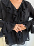 Close-up of black blouse sleeve and front tie with soft ruffled edges.