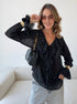 Woman wearing black sheer blouse with ruffled neckline and gold accessories.