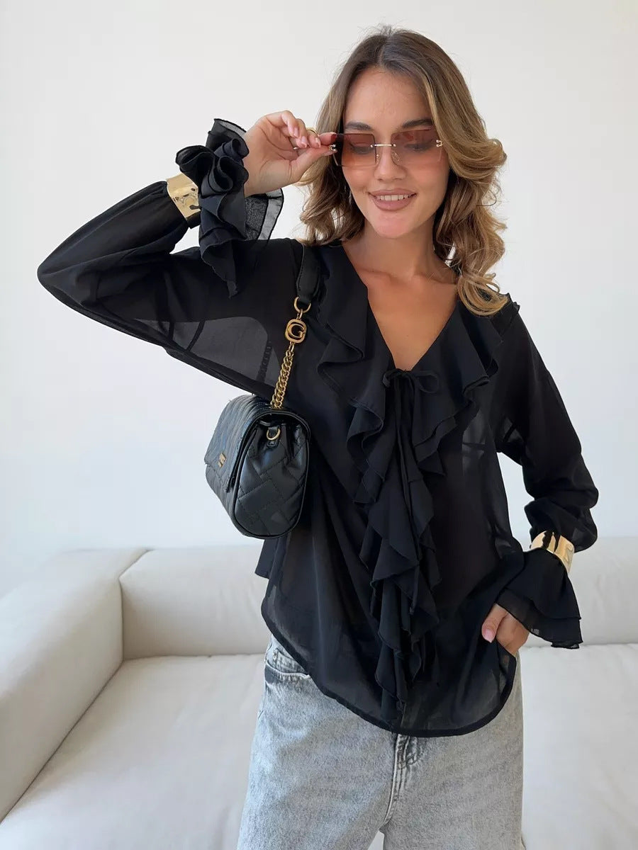 Woman wearing black sheer blouse with ruffled neckline and gold accessories.