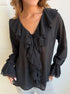 Black ruffle blouse with V-neckline and layered trim details.