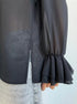 Side view of black blouse hem with slit and ruffled sleeve