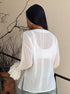 Back view of sheer white long sleeve blouse with flared cuffs.